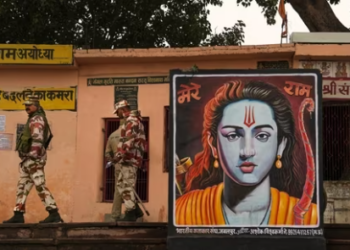Security personnel walk past a poster of Lord Ram, ahead of the consecration ceremony of Ram Mandir, in Ayodhya, on January 20.(PTI)