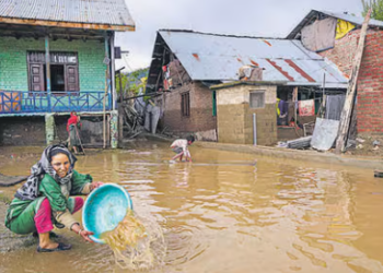 A woman removes standing water from her partially submerged house as flood water recedes at Chogal Handwara, in Kupwara district of North Kashmir
